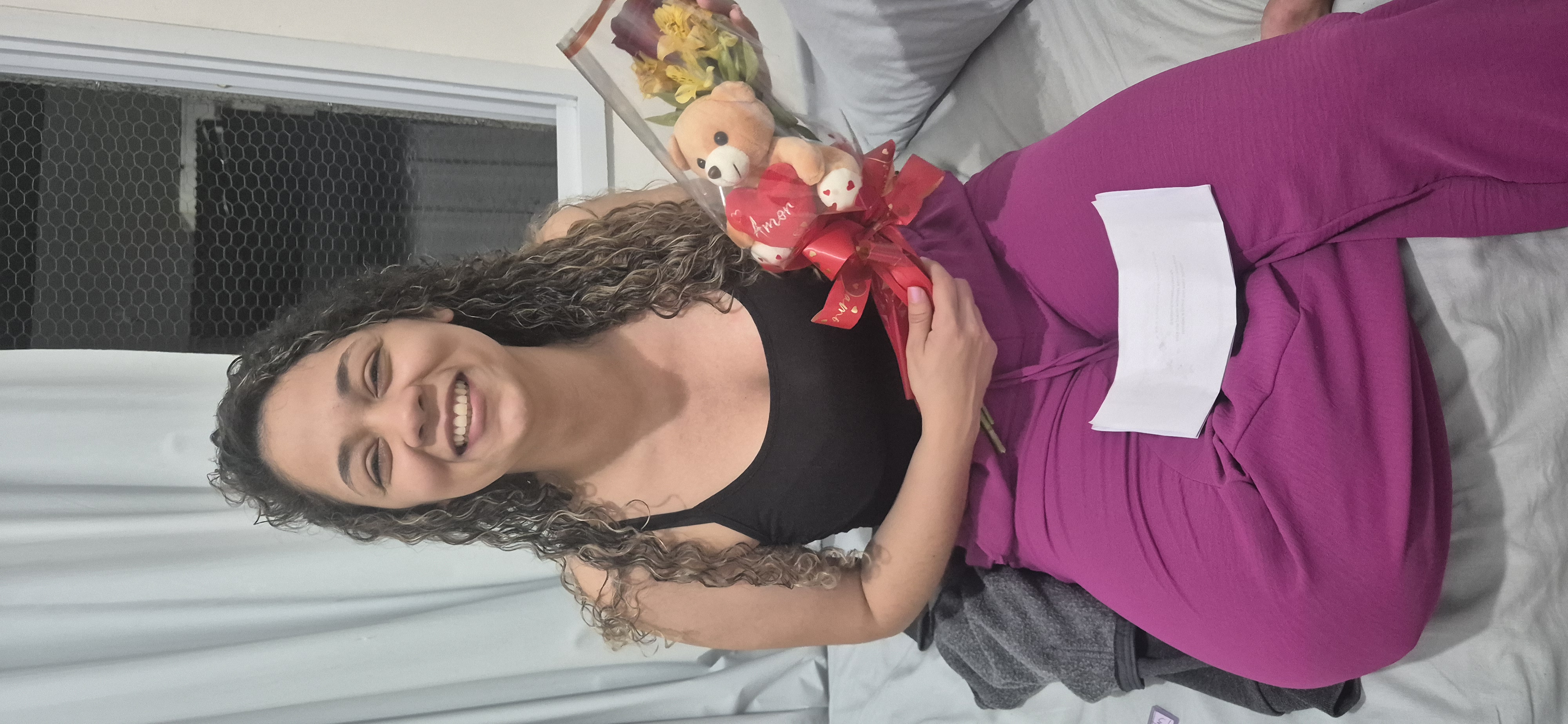 Raíla sorrindo com um buquê de flores e ursinho